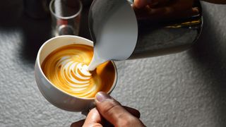 A person doing latte art in a white cup